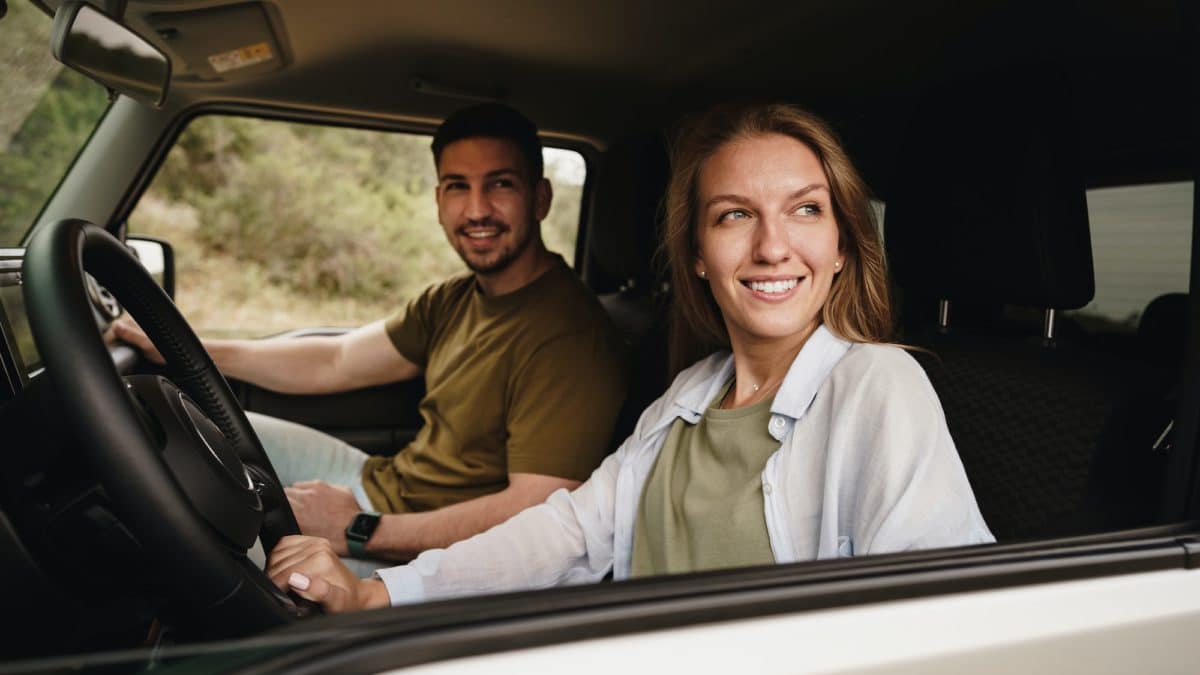 Beautiful young couple sitting on front passenger seats and driving a car