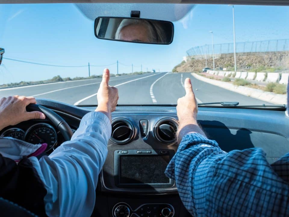 couple of seniors driving and having fun together with a rent car in the street - two pensioners